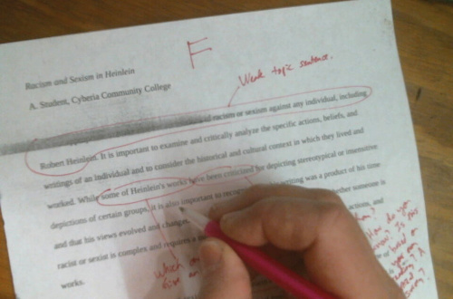 Hand grading a paper with a red pen. The paper has an F at the top.