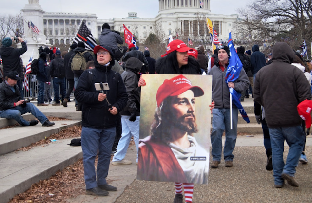 A woman holds a sign showing Jesus in a MAGA hat.